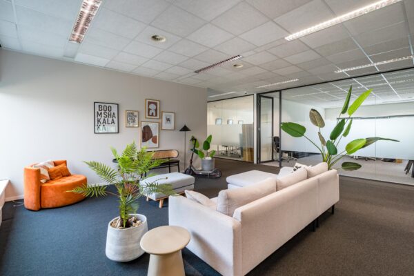 Moderne loungehoek in een kantoorpand aan het Rivium Boulevard, met comfortabele zitmeubels, kamerplanten en glazen vergaderruimtes op de achtergrond.